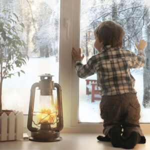 Young Boy Comfortable Inside Looking Through A Window At The Snow